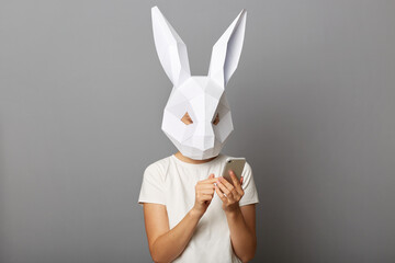 Indoor shot of female wearing bunny mask and orange sweatshirt posing isolated over gray...