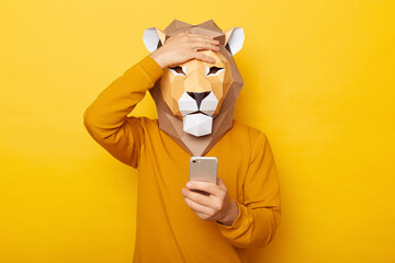 Photo of sad upset male wearing lion mask and orange sweatshirt posing isolated over yellow...