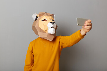 Portrait of anonymous man blogger wearing lion mask and orange sweatshirt isolated over gray...