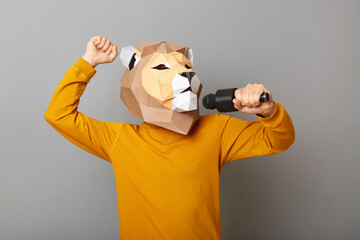 Portrait of festive funny anonymous man wearing lion mask and orange sweatshirt isolated over gray...
