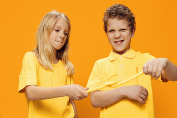 Obraz premium cute, happy children brother and sister, standing in bright yellow clothes fighting with their lollipops. Studio horizontal photography on orange background