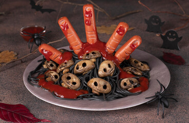 Themed food for Halloween - bloody hand from sausages with ketchup, mushrooms in form of skulls and black italian pasta - obrazy, fototapety, plakaty