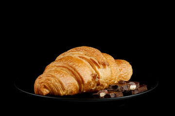 Croissant with pieces of chocolate on a black plate.
