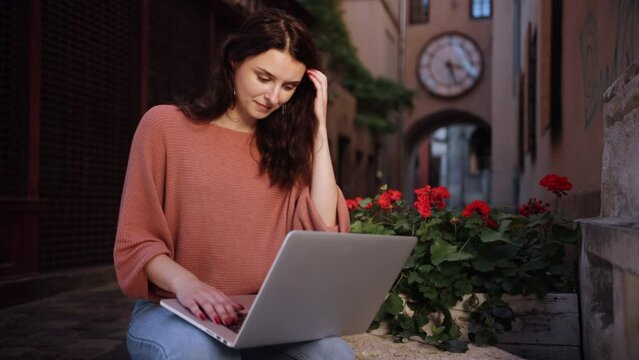 A student studying outdoors, a freelancer working on the decorative stone of city streets, a beautiful happy smiling romantic woman blogger working on a laptop online