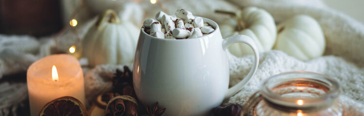 Autumn cozy home composition with hot chocolate with marshmallow and candles. Aromatherapy on a grey fall morning, atmosphere of cosiness and relax. Wooden background close up banner copy space