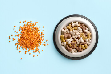 Dry dog vegan vegetarian food concept. Red lentils near bowl with pet feed on blue background