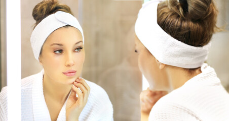 woman looking in the mirror in the bathroom and taking care of her skin.Applying the cream	.Magic anti-aging cream.