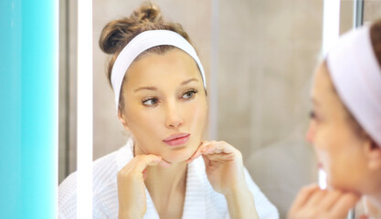 woman looking in the mirror in the bathroom and taking care of her skin.Applying the cream	.Magic anti-aging cream.