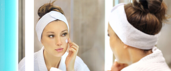 woman looking in the mirror in the bathroom and taking care of her skin.Applying the cream	.Magic...