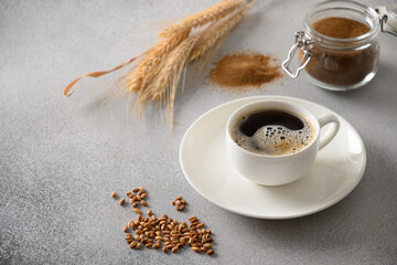 Barley coffee in white cup, beans and ears of barley on gray background. Great warming caffeine free drink alternative coffee. Close up.