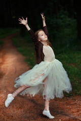 Pretty little slim girl dancing as ballet dancer ballerina on a road in summer forest with dark background, dressed in white fluffy dress and ballet shoes, leisure outdoor portrait, vertical  © upparadox