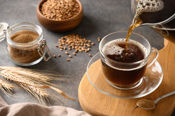 Pouring barley coffee in glass cup on brown background. Cooking healthy caffeine free alternative coffee. Close up.