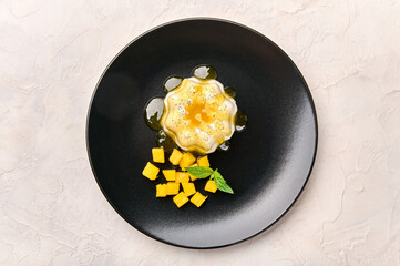 Flat lay panna cotta homemade with natural vanilla pod, mango syrup and mint on black plate