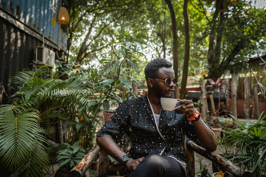 a black man holding in tea cup in a garden 