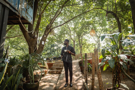 black man wearing a kimono posing for a portrait while holding a tea cup in a garden