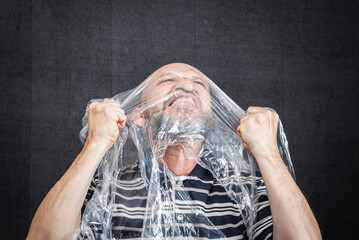 Mature man with a transparent plastic bag flying over his head and face.