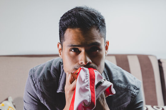 Joven fan&aacute;tico del f&uacute;tbol, gritando gol, apoyando a su equipo sentado en el sof&aacute; de casa viendo la transmisi&oacute;n en vivo del encuentro. Concepto de mundial de futbol e hinchas del futbol en el mundo.