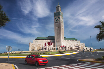 view of Hassan II Mosque and a red taxi passing near it. famous landmark. public transport