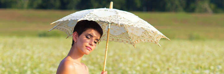 Young elegant woman with parasol walking on the meadow grass amongst flowers on a sunny summer day © Solid photos