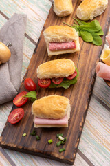 small sandwiches of ham, salami and cheese with tomato and arugula for fruit buffet with homemade seed bread on a wooden board and different sauces