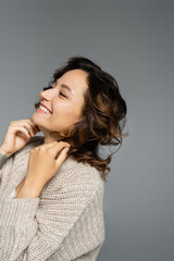 cheerful brunette woman with wavy hair smiling isolated on grey