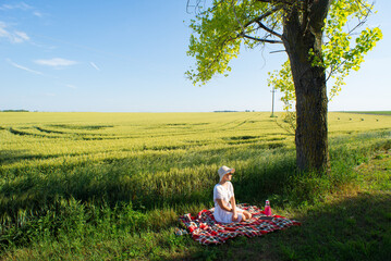 Young woman on the picnic sitting beside wheat field on a sunny spring day