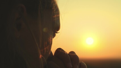 girl prays looking sunset, long hair flying away in glare sunlight rays strong wind, looking at dawn, lonely hike of brave girl, looking into sky with her eyes, believing good. close-up hands face.