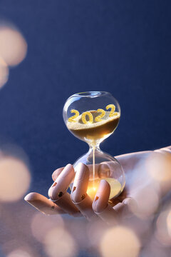 End of the year 2022, Silverster, Happy New Year 2023. Hourglass with numbers 2022 and 2023 and light garland on dark blue background. Hourglass is also known as sandglass, sand glass, sand timer or