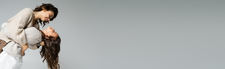 side view of trendy and cheerful woman dancing with daughter isolated on grey, banner