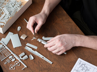 Person is assembling several small pieces to make the final aircraft model. Parts of plastic model airplane in man's hands