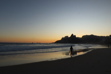 Fototapeta na wymiar Rio de Janeiro, RJ, Brazil, 2022 - People walking in silhouette at Ipanema Beach at sunset