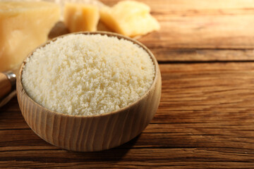 Bowl with grated parmesan cheese on wooden table, closeup. Space for text