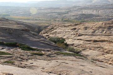 Layered slopes of the volcanic plateau in the Bektau-Ata tract with a distant view, with green bushes, in the sunlight at sunset