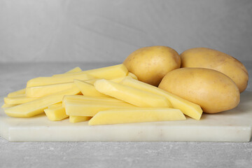 Whole and cut raw potatoes on light grey table, closeup. Cooking delicious French fries