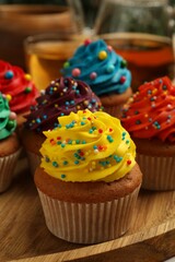 Delicious cupcakes with colorful cream and sprinkles on wooden board, closeup