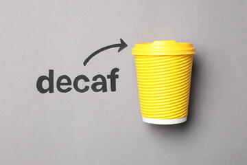 Word Decaf and arrow pointing at takeaway paper coffee cup on light grey background, top view