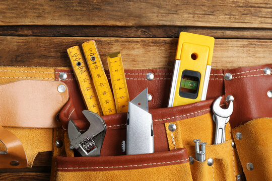 Belt with utility knife and different tools on wooden table, top view
