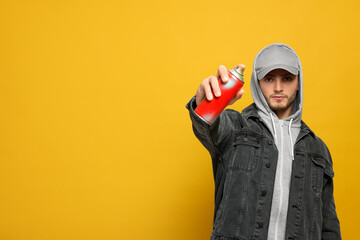 Handsome man holding can of spray paint on yellow background. Space for text