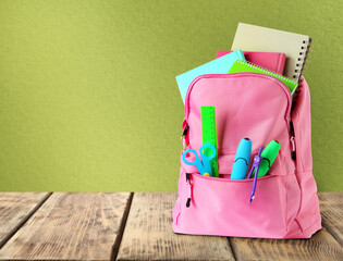 Backpack with school stationery on wooden table against green background, space for text