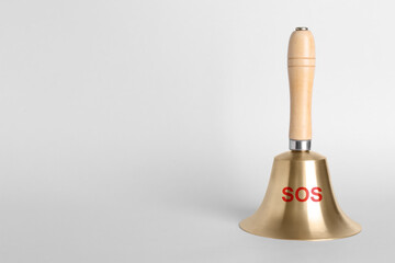 Golden bell with wooden handle and abbreviation SOS on grey background. Space for text