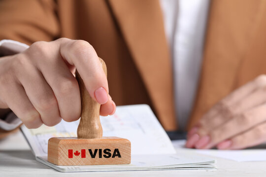 Woman Stamping Document At White Wooden Table, Closeup. Visa For Canada