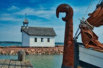 Small wooden church on an island with a viking ship at the docks with a dragon's head on the prow