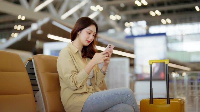 Asian woman waiting for departure at the airport on vacation holiday. Asia female passenger using mobile smart phone and sitting in terminal hall while waiting for her flight