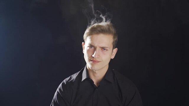 Smoke is coming out of the angry man's head.
Frustrated young man is angry and smoke is coming out of his head.
