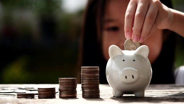 A Idea to Help You Save Money. Asian female toddler saving money by stacking coins in glass jar, outdoors in the sunshine. Concept of save money, education, finance, bank, investment, business, growth
