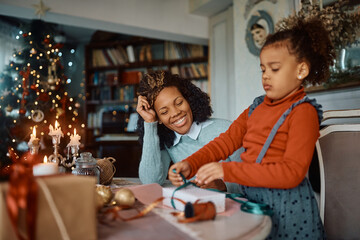 Happy black mother enjoys in preparing presents for Christmas with her small daughter.