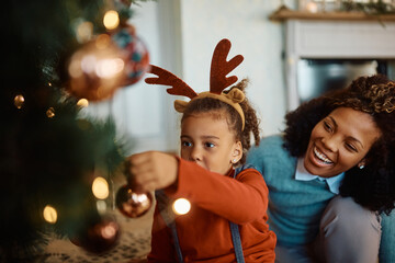 African American mother and daughter enjoying while putting ornaments on Christmas tree.