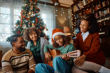 Black girl plays acoustic guitar to her extended family during Christmas day at home.