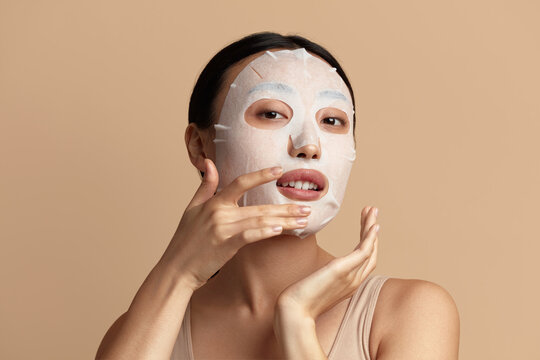 Woman Face Mask. Portrait Of Beautiful Girl Applying Cosmetic White Textile Mask at Facial Skin. Closeup Of Attractive Young Woman With Natural Makeup And Cosmetic Mask On Face. High Resolution 