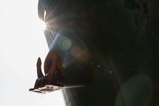 The sun glares down on a large ship anchor, seen on an industrial bulk carrier.